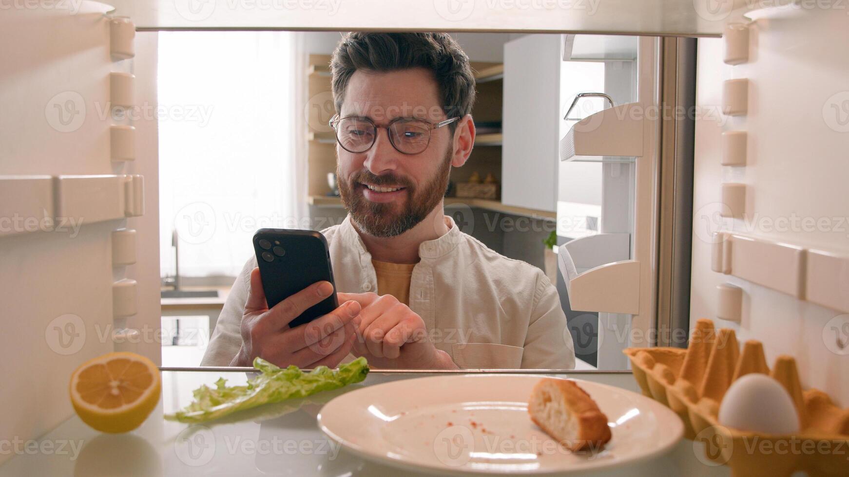 Hungry man guy open empty refrigerator poor crisis order food delivery with smartphone online buying products ordering goods with mobile phone store cellphone app point of view POV from inside fridge photo