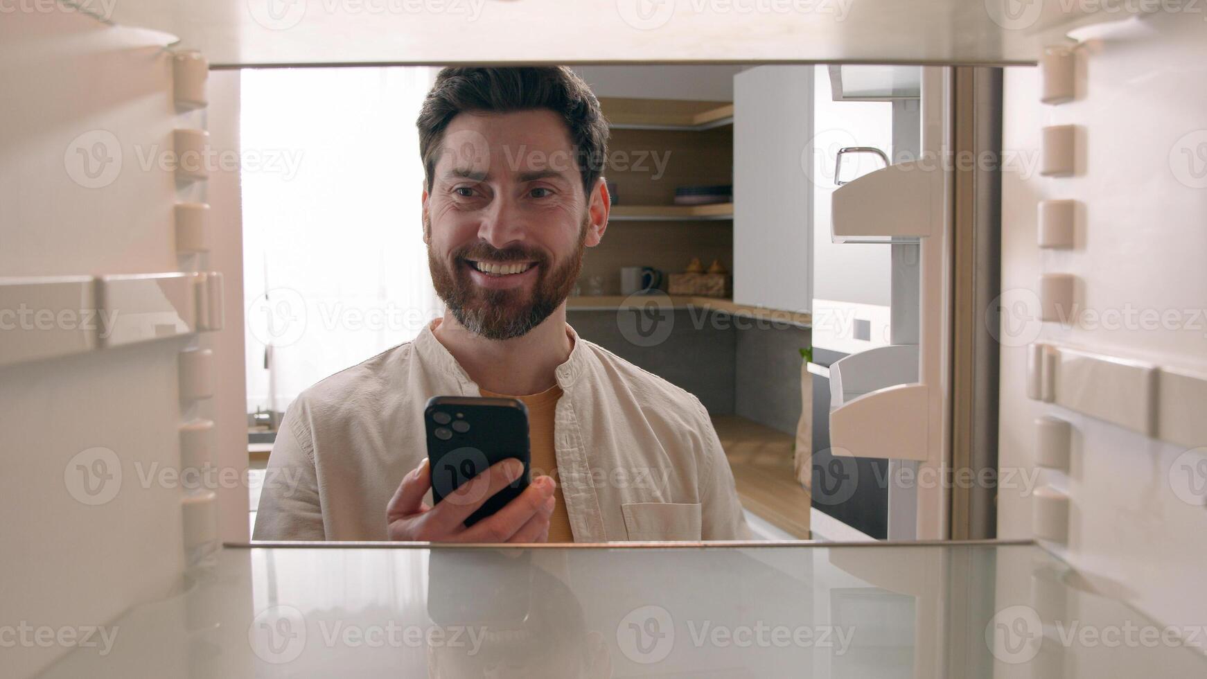 Hungry man guy open empty refrigerator poor crisis order food delivery with smartphone online buying products ordering goods with mobile phone store cellphone app point of view POV from inside fridge photo