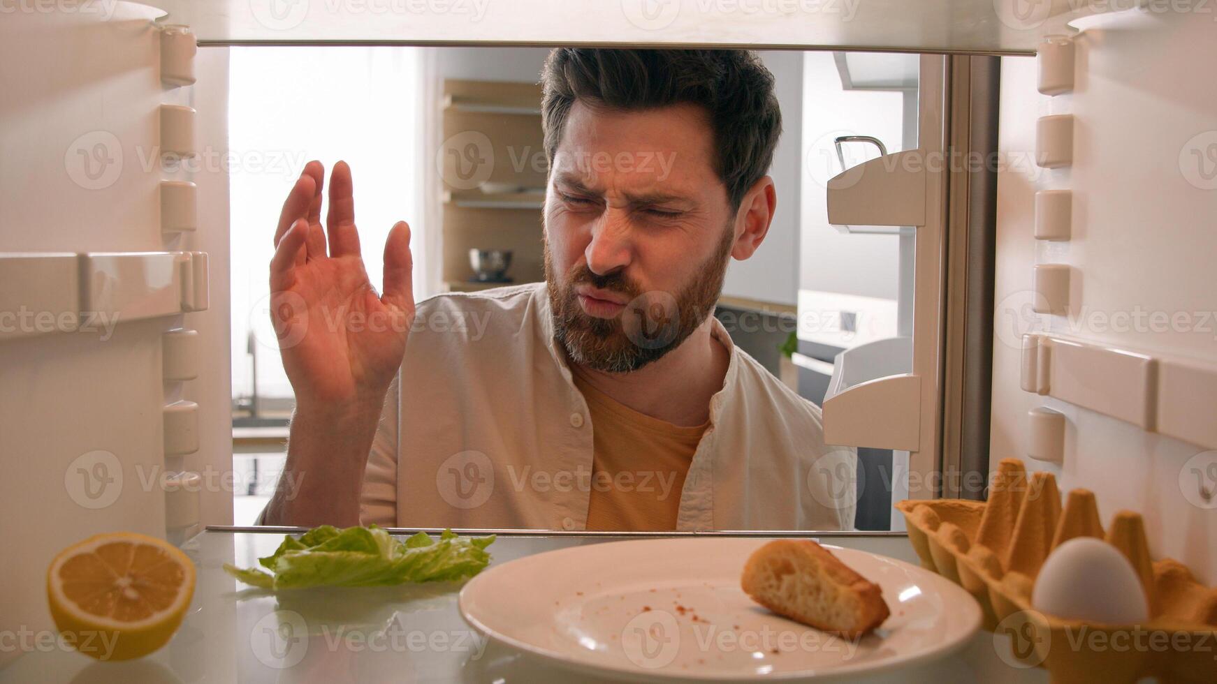 Point of view from inside refrigerator POV Caucasian adult man householder homeowner open fridge door kitchen smell awful smelling guy bad aroma nausea confused odor disgust spoiled food salad leaves photo