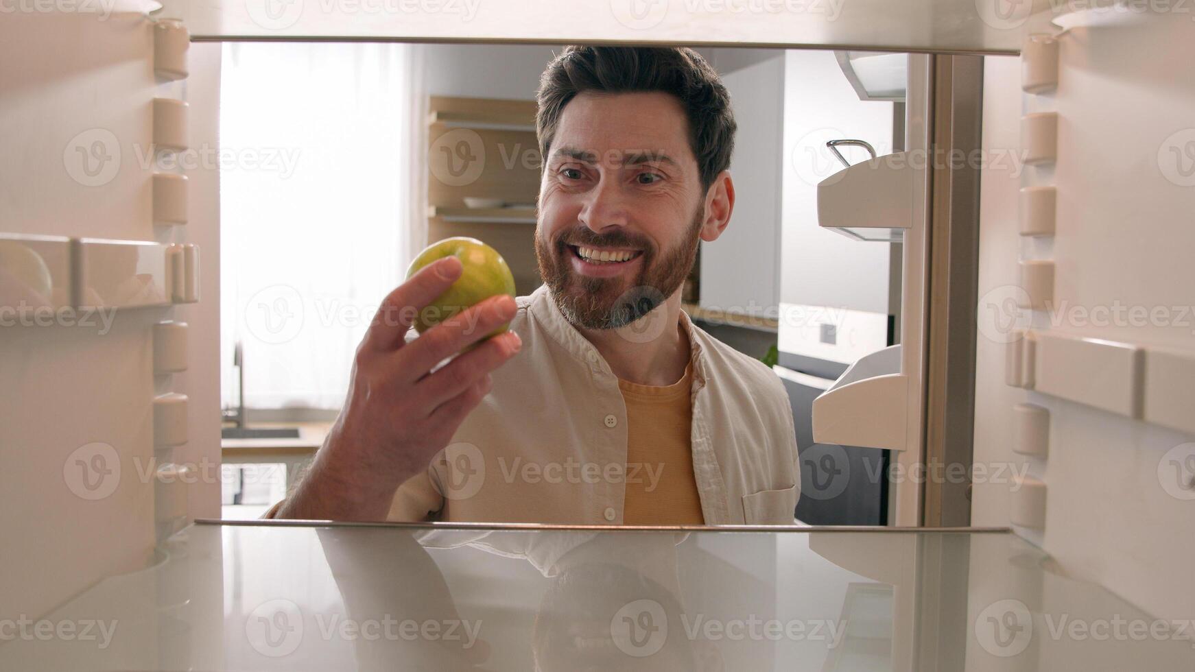 POV point of view from inside refrigerator Caucasian adult happy man at kitchen open empty fridge take last green apple bite eat fresh healthy fruit hungry guy male eating diet food delivery service photo