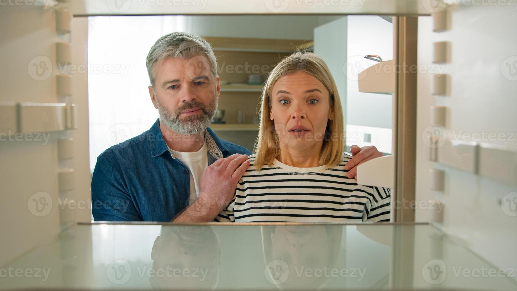 Point of view POV from inside refrigerator Caucasian adult family mature couple middle-aged man woman open empty fridge have nothing to eat sad upset with poor poverty unemployment starvation hunger photo
