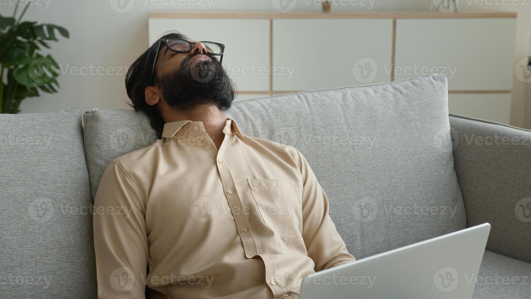 Tired exhausted freelancer working with laptop at home overworked Arabian muslim man fall asleep on couch sick weary sleeping Indian businessman lean on sofa exhaustion fatigue need break rest relax photo