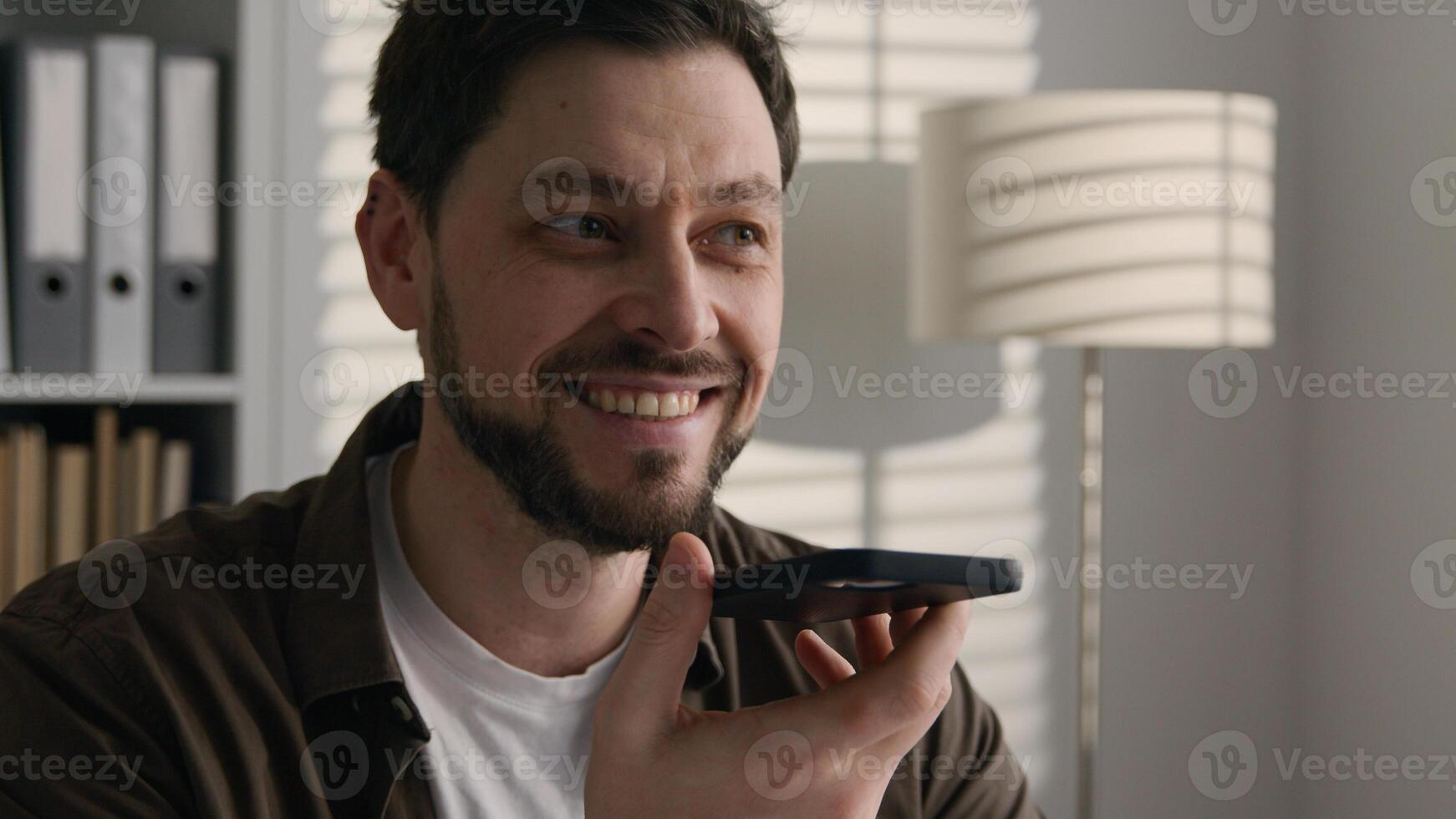 Smiling happy Caucasian man recording voice audio message send voicemail talk mobile phone loudspeaker business call in office businessman make heart love shape support symbol thanking love feelings photo