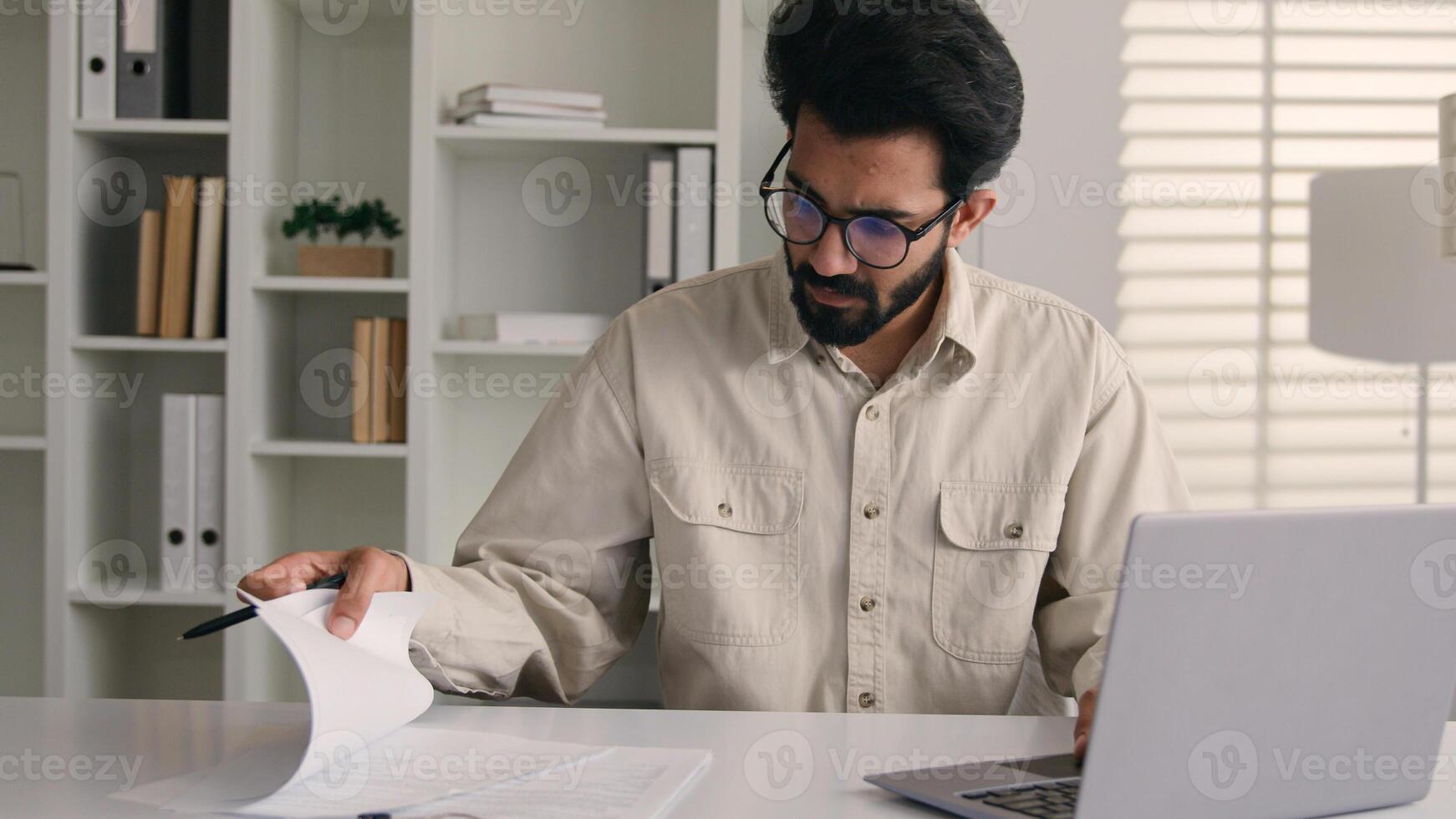 Focused man Arabian Indian ethnic businessman male employee manager writing notes business tasks data paperwork signing documents write on papers counting budget working with laptop computer in office photo