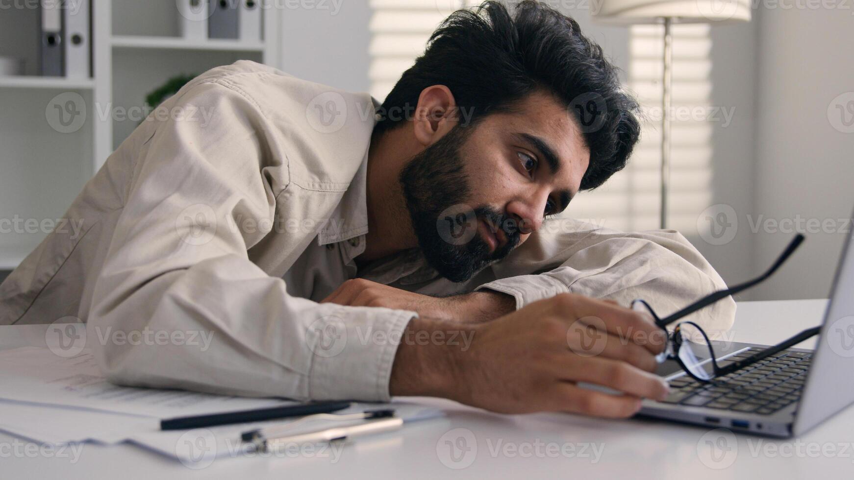 Lazy weary sleepy male manager tired exhausted Arabian Indian businessman employee working computer boring remote job man fall sleep on desktop napping in office overwork fatigue no energy sleeping photo