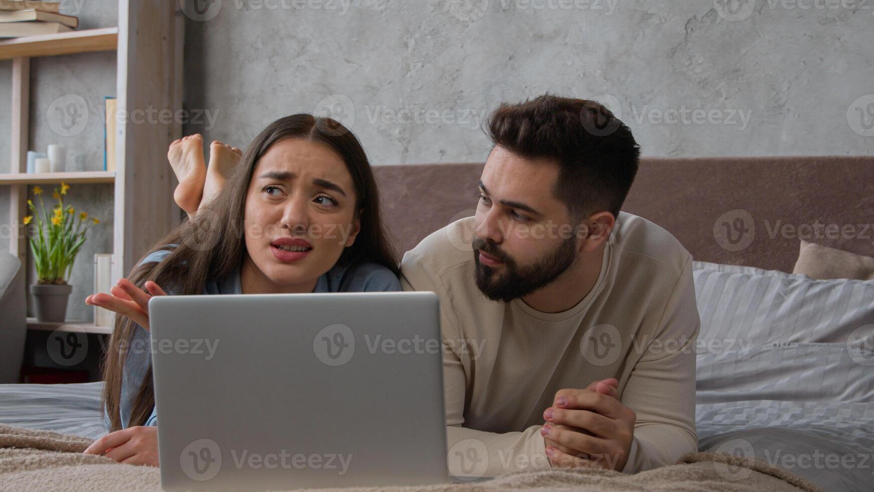Caucasian couple married wife husband lying on bed family talking discuss shopping online together use laptop internet order young woman man clients looking at computer choosing home goods for bedroom photo