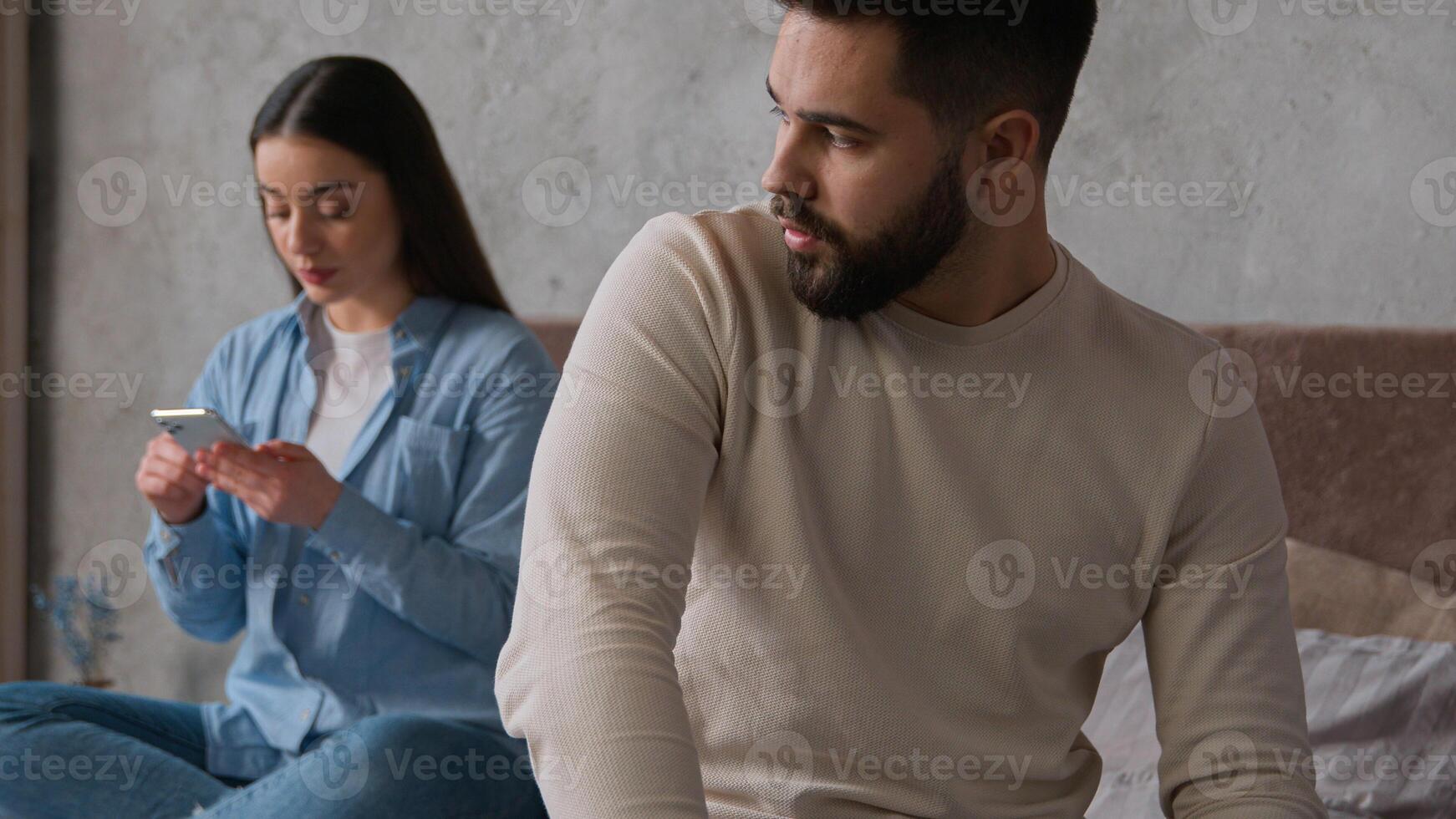 Caucasian couple problem relationship sad upset man sit separate from woman on bed offended on wife addicted gadget scrolling mobile phone smartphone ignoring husband internet social media addiction photo