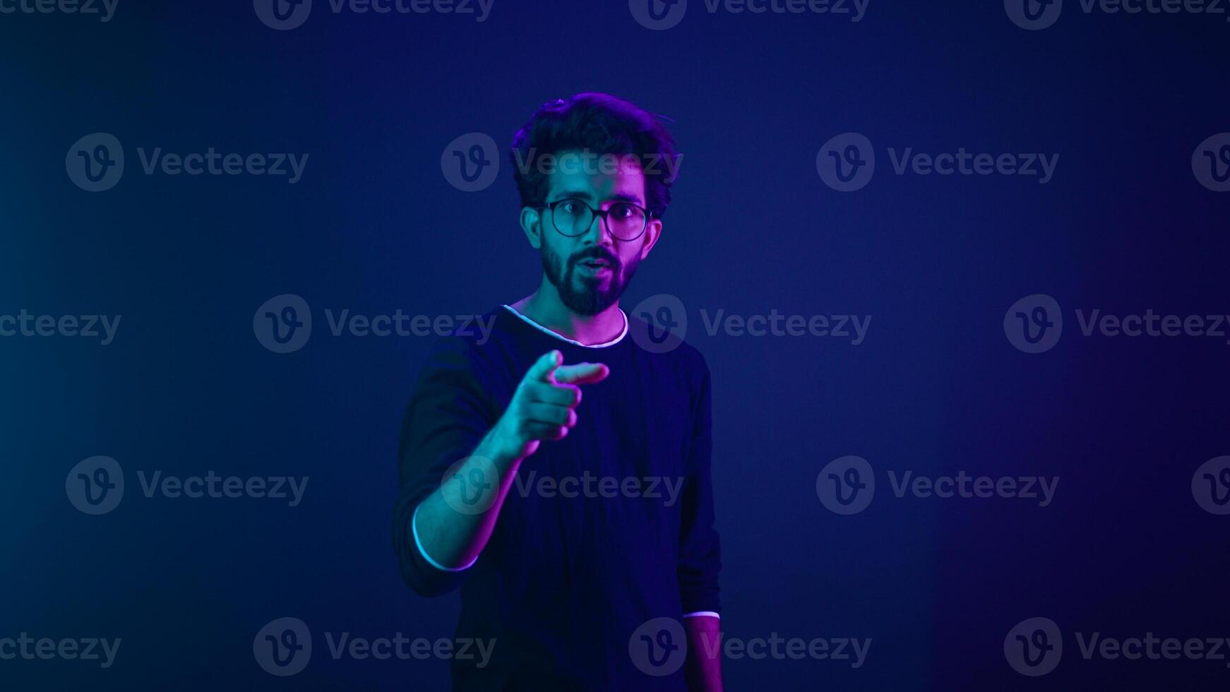 Neon ultraviolet background happy Indian guy Arabian man worker coder hacker computer engineer showing hey gesture pointing at camera smiling satisfied show thumbs up support good idea agree recommend photo