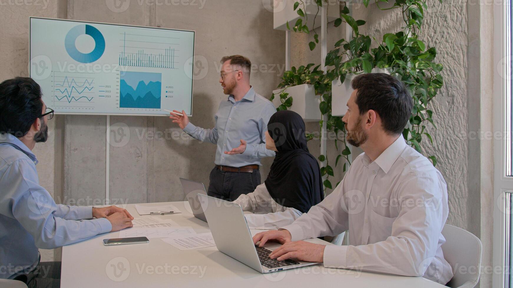 Office team leader man mentor show charts financial growth graphics presentation on interactive board diverse businessmen and muslim businesswoman in hijab discussing project group conference meeting photo