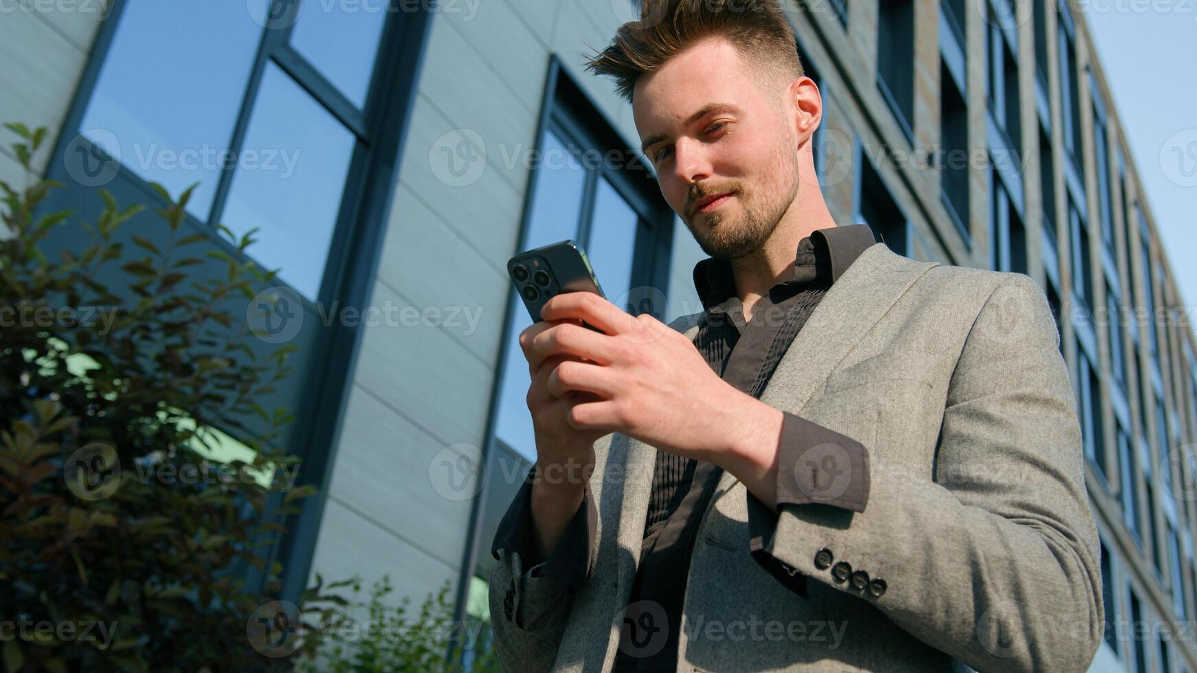 Smiling pensive caucasian man businessman entrepreneur browsing social network using mobile phone walk street near office building happy male client check email send SMS message on smartphone outdoors photo