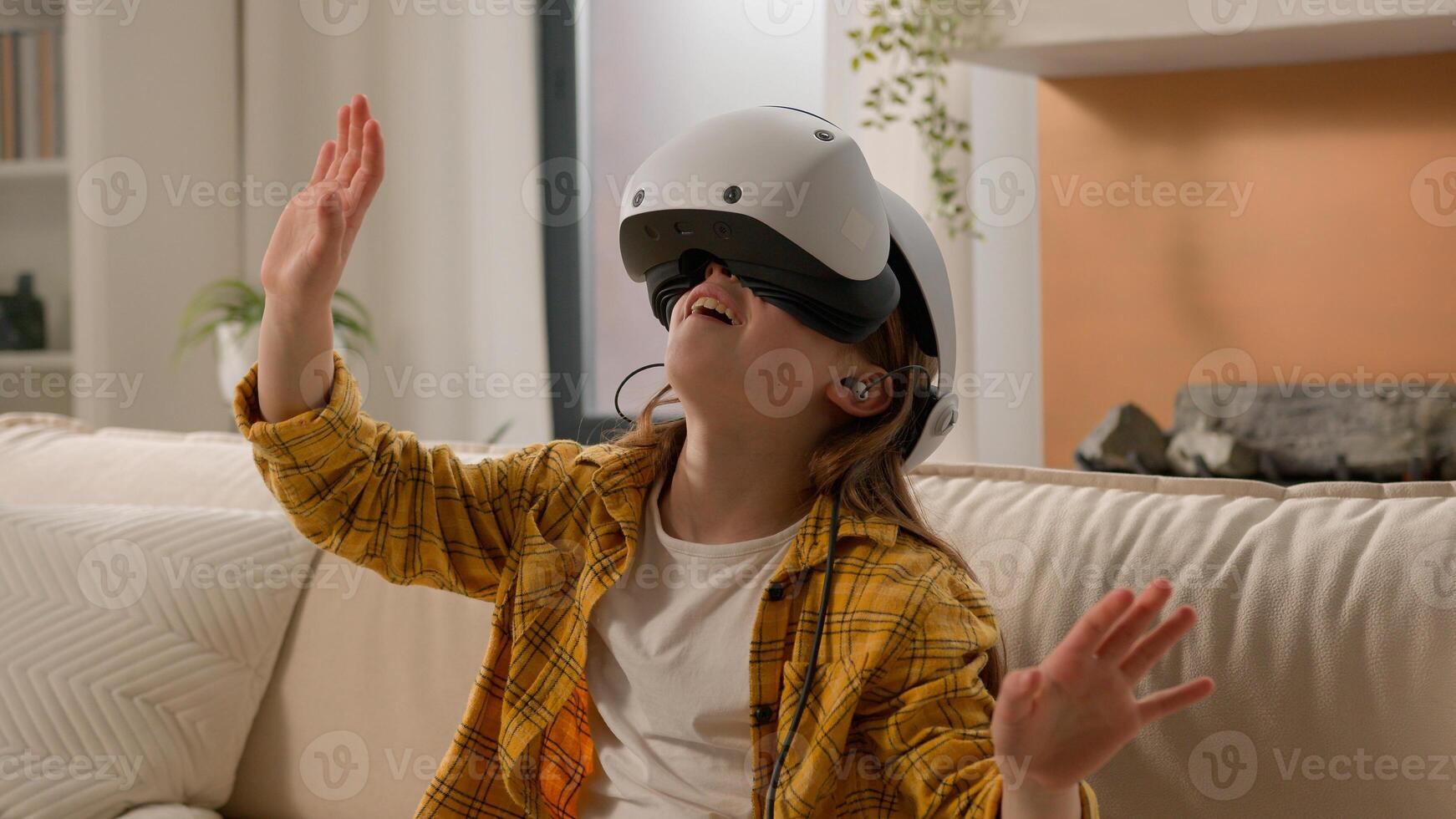Funny caucasian kid girl child schoolgirl having fun in virtual reality headset at home couch playing online game in world metaverse using innovative technology VR glasses exploring cyberspace photo