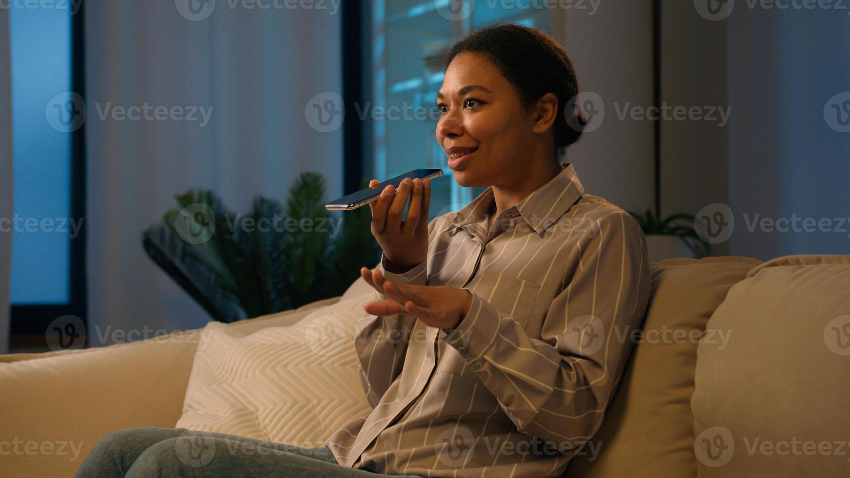 African American woman businesswoman record voice message on speaker phone send audio voicemail dictate information in microphone AI mobile assistance speak cellphone talk loudspeaker at evening home photo