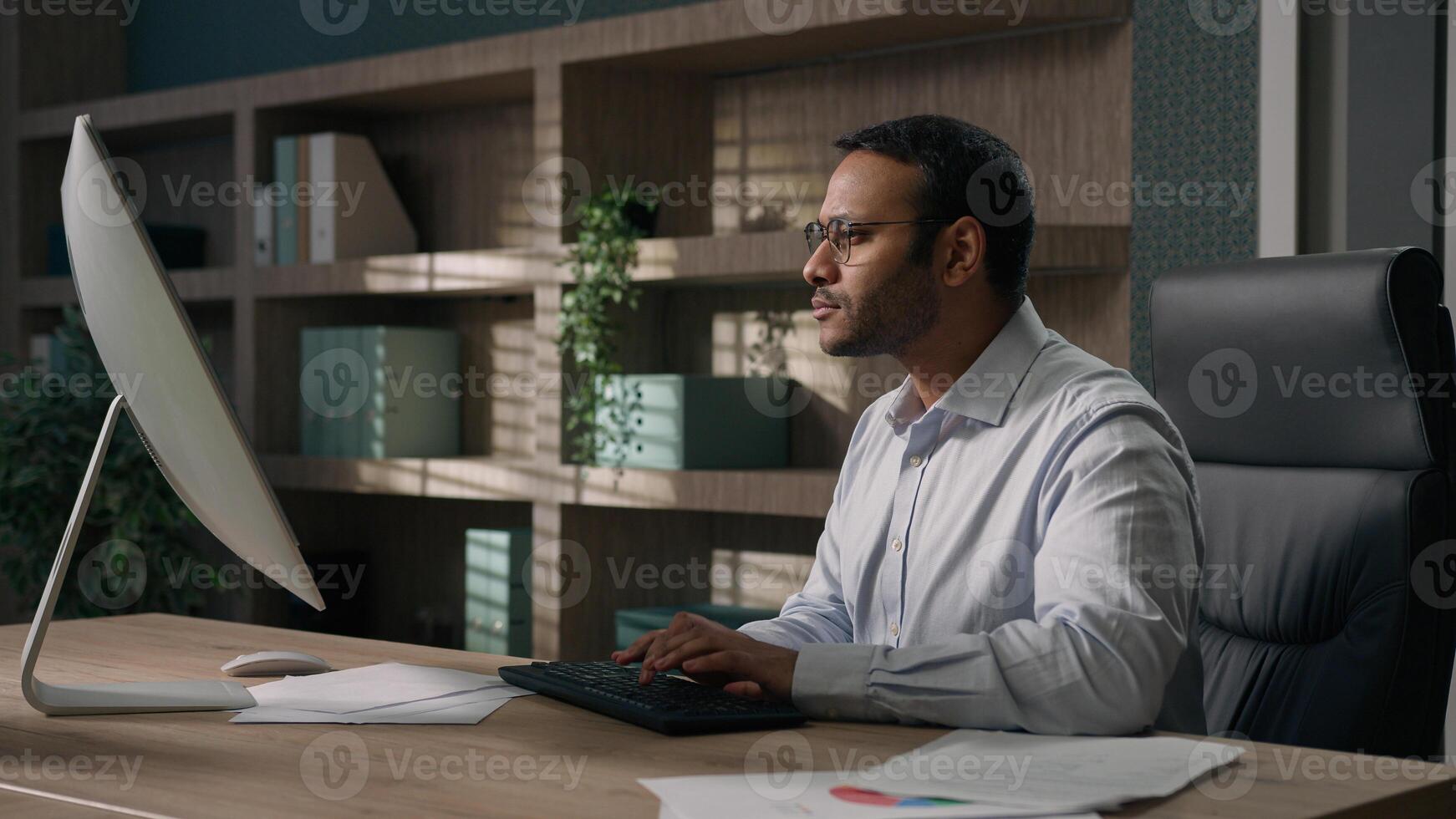 Indian man in glasses Arabian businessman American worker employer typing chatting working in office computer corporate software business project coder programming touch eyeglasses busy at workplace photo