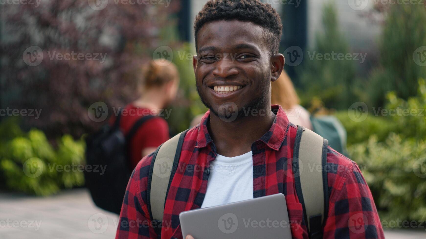 Happy African American student guy man male schoolboy in city outdoors university college campus smiling to camera smile enjoy education study knowledge generation Z students talking on background photo