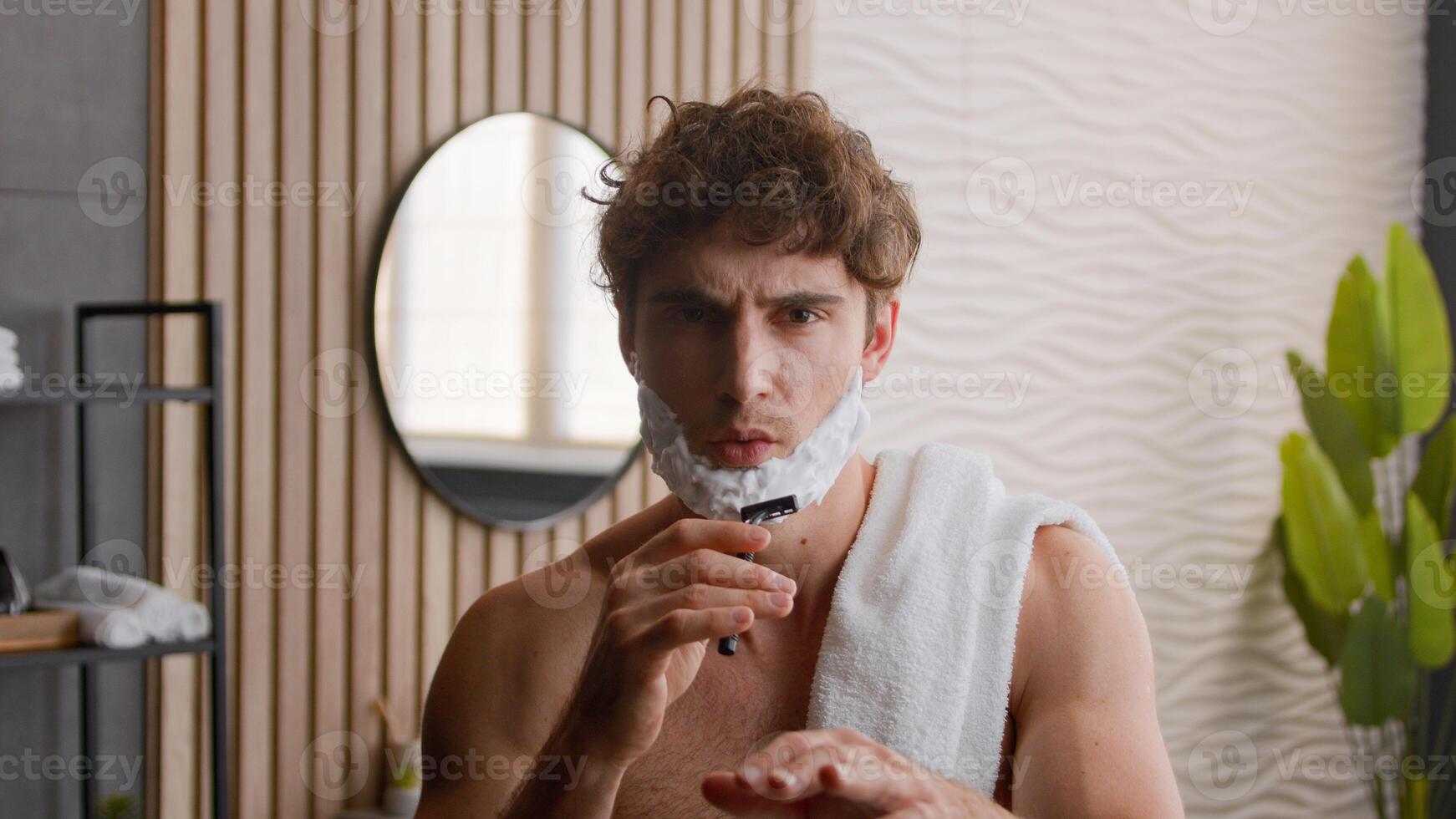 Caucasian millennial guy man funny carefree comical humorous male with foamy beard with shaving gel foam on face singing song in shave razor sing dancing having fun grooming procedure morning routine photo