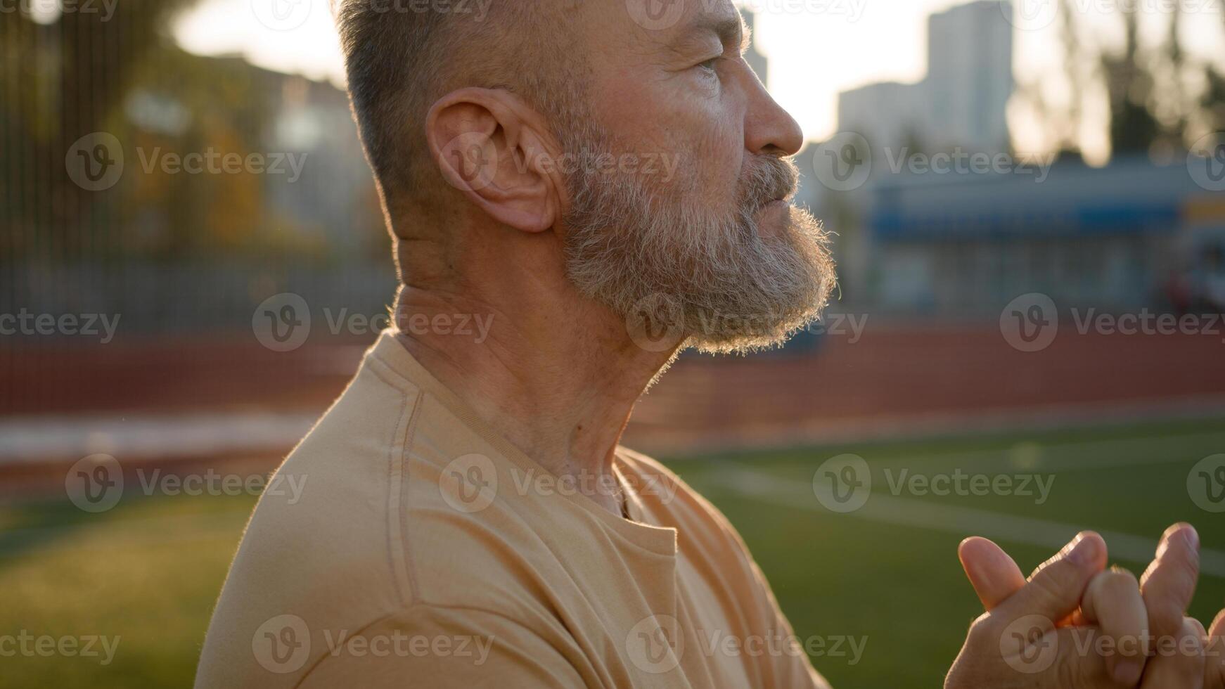 Old Caucasian man stretch hands before training warm-up stadium outside city sportsman sport lifestyle sunray stamina physical activity wellness motivation bodybuilder flexibility aerobics exercising photo