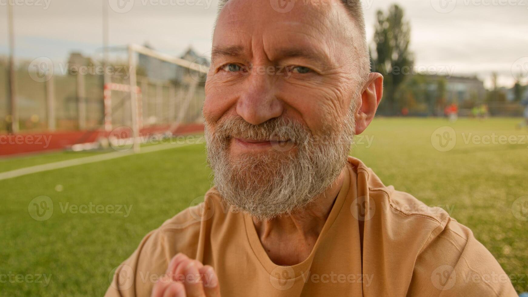 Old elderly Caucasian man stadium outside meditating on lawn sitting closed eyes smiling harmony retirement concentration wellness dreaming peaceful exercise balance fitness gymnastics posture sport photo