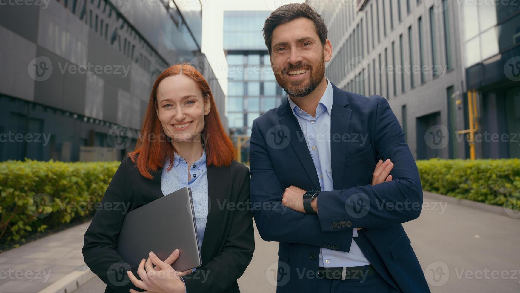 Caucasian successful confident happy businesspeople business woman man looking at each other smiling look at camera posing hands crossed in city outdoors office building colleagues coworkers partners photo