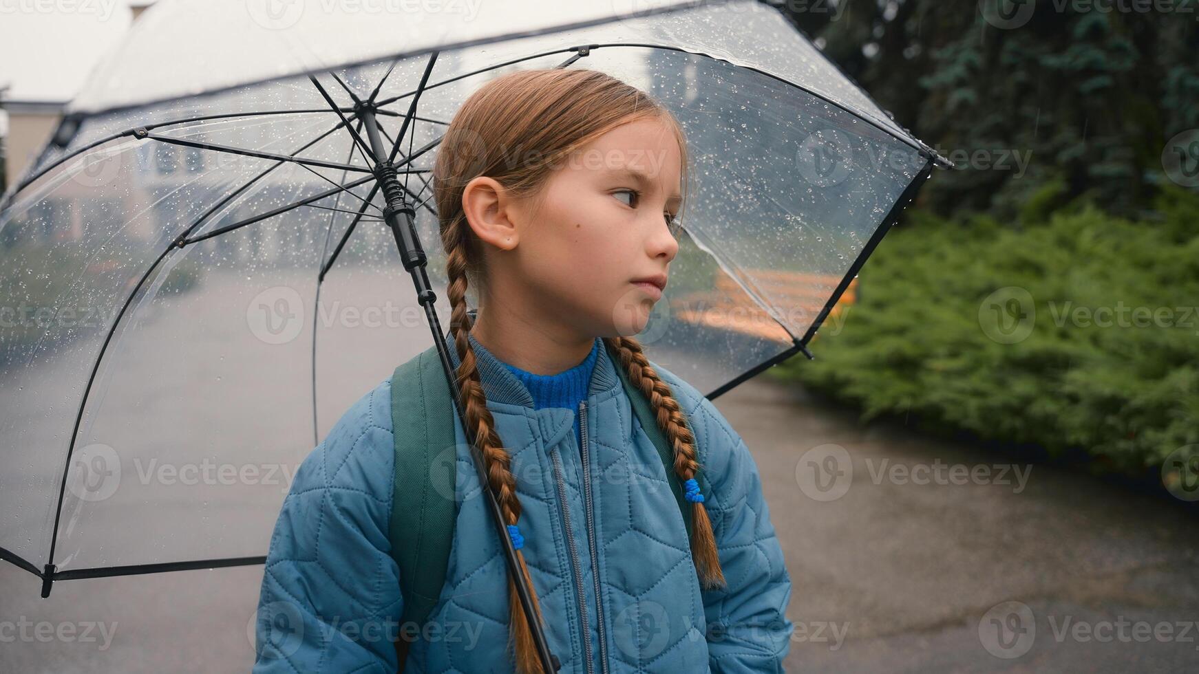 Tired little girl schoolgirl child looking at camera bored unhappy bad weather rain umbrella city park outdoors fatigue damp wet face daughter kid pupil offspring lonely sadness rainfall discomfort photo