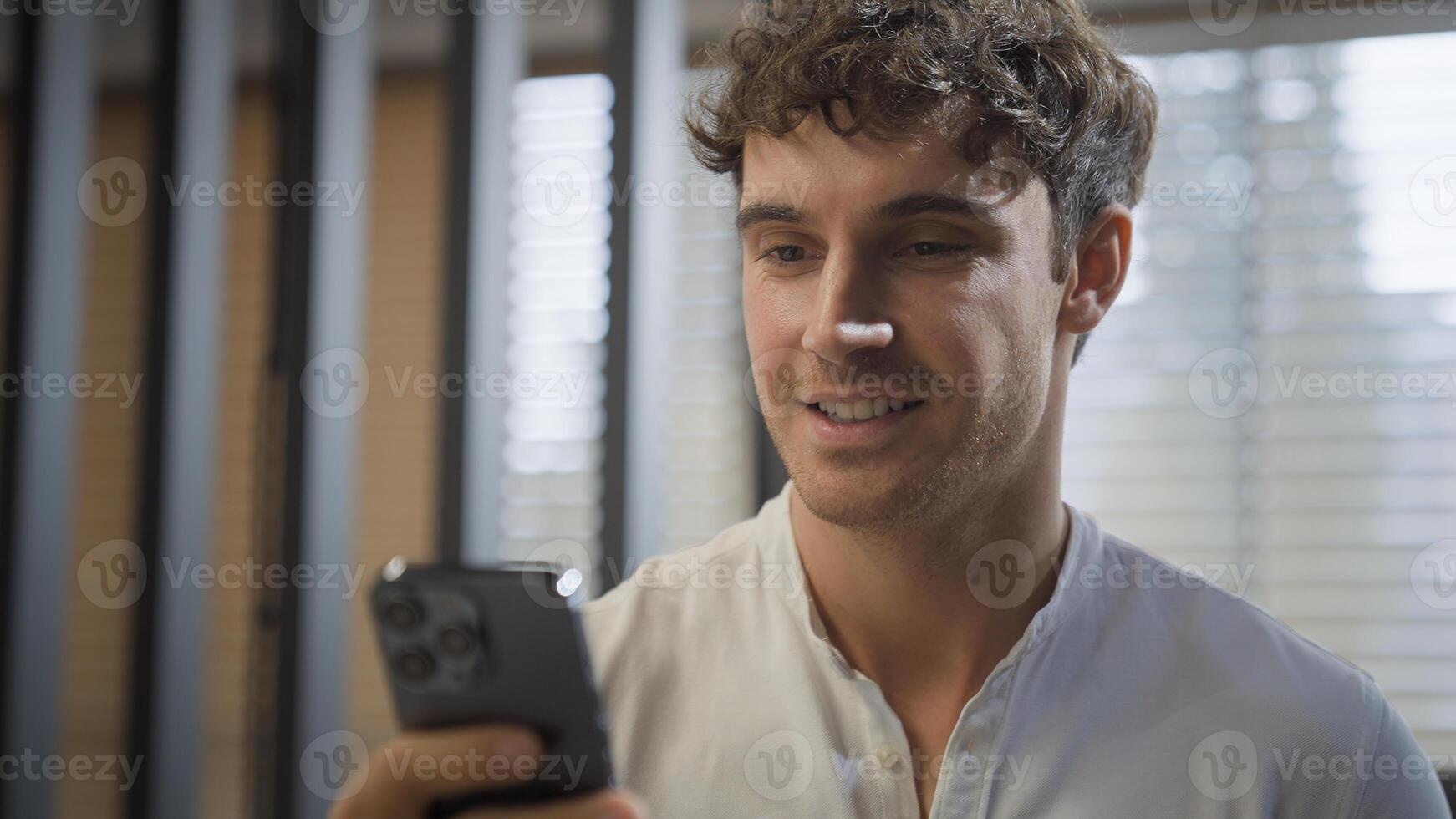 Caucasian smiling happy businessman walking in office looking at smartphone reading good news message business man smile go in company indoors hold mobile phone professional online communication chat photo