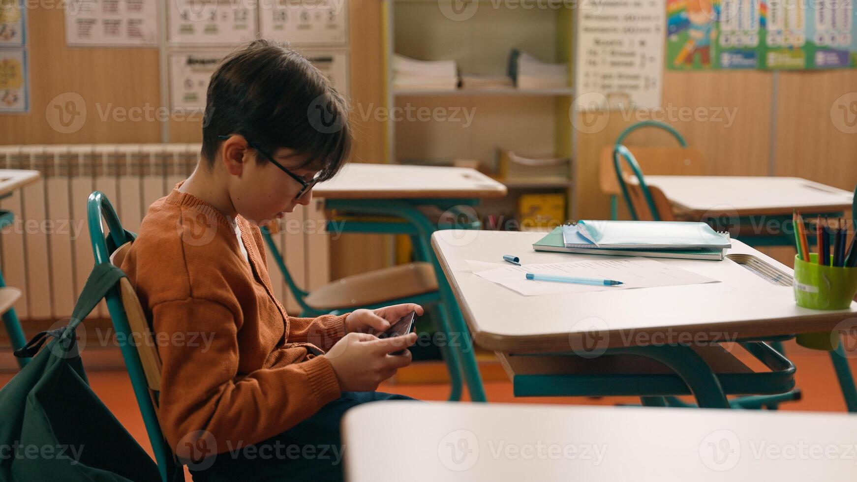 Child kid son pupil student bad behavior boy schoolboy playing game on mobile phone at lesson at school hide smartphone under class desk distract from studying gadget addiction writing learning photo