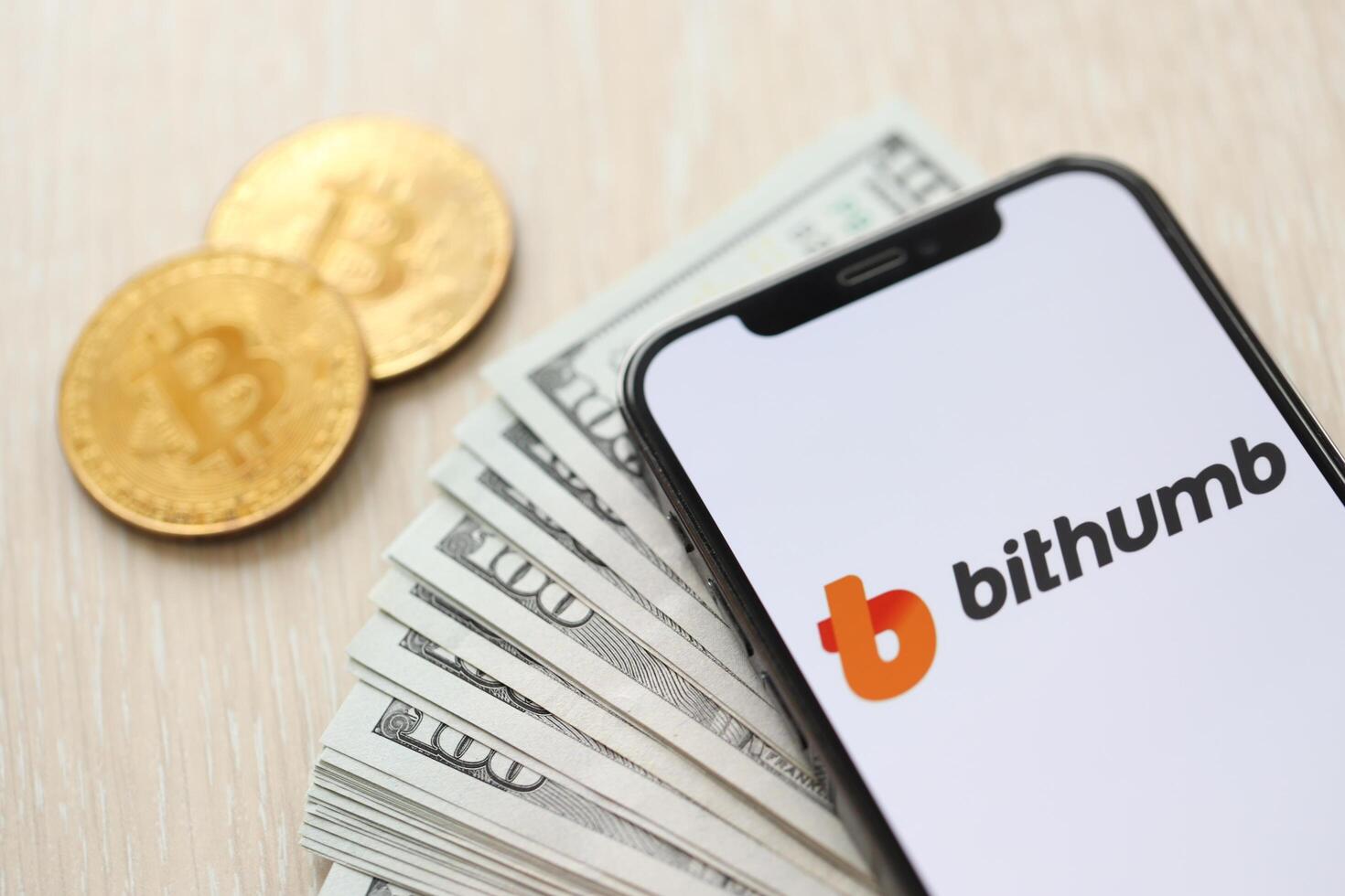 KYIV, UKRAINE - MARCH 15, 2024 Bithumb logo on iPhone display screen with dollars and bitcoins on table photo