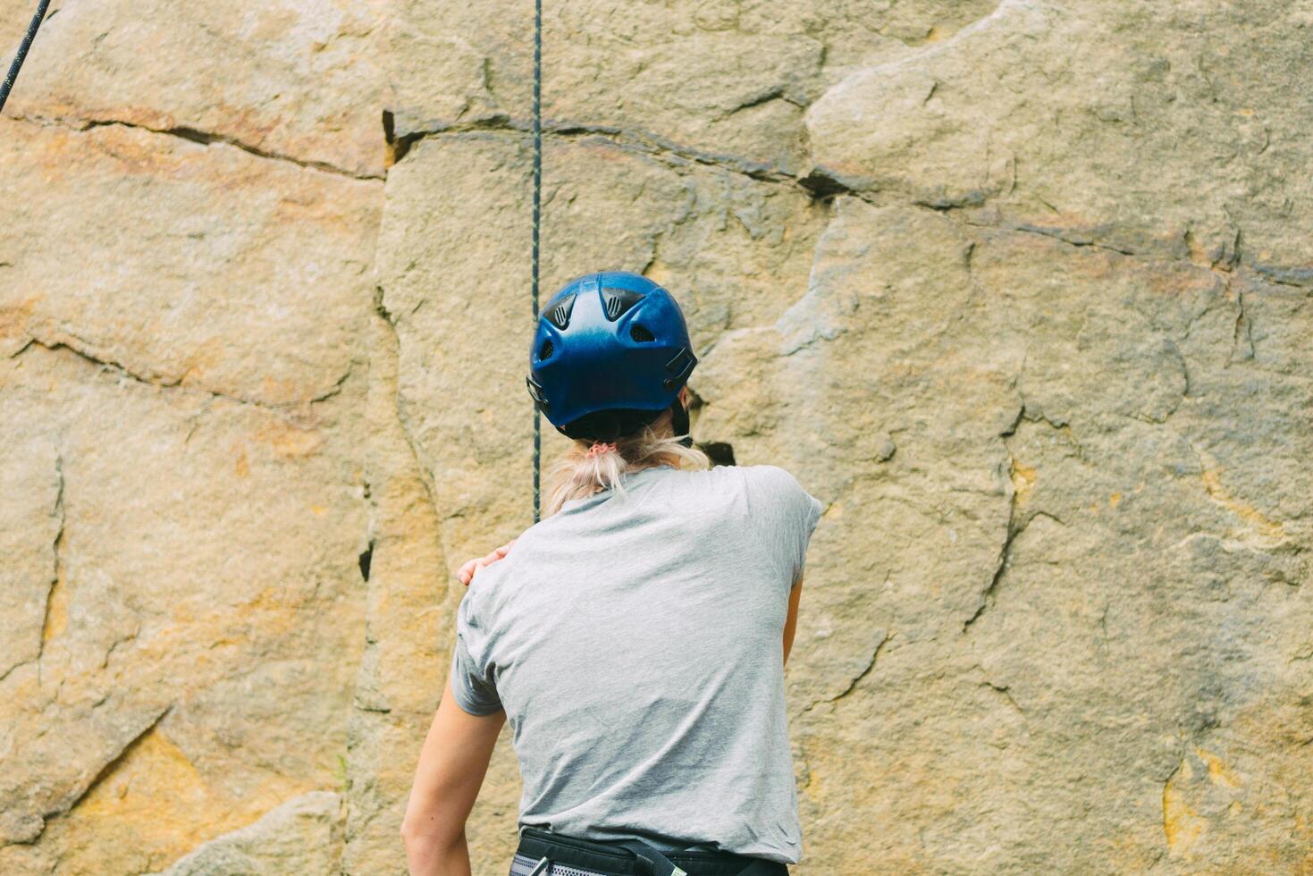 Young athletic woman in equipment standing in front of stone rock outdoors and getting ready to climb. Training area for outdoor activities. Extreme sport. Rear view photo
