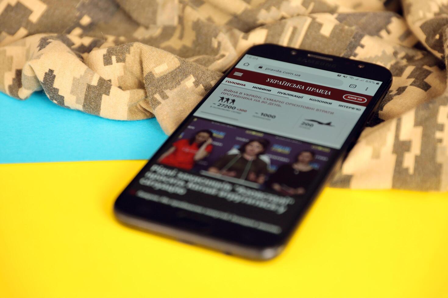 KYIV, UKRAINE - 4 MAY, 2023 UP Ukrainska Pravda ukrainian news portal on smartphone screen with ukrainian flag and camouflage fabric photo