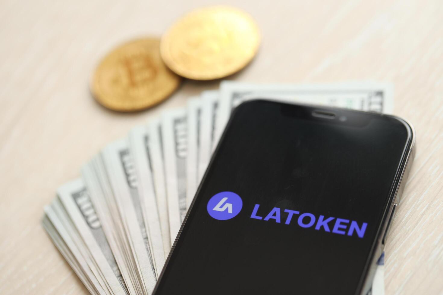 KYIV, UKRAINE - MARCH 15, 2024 Latoken logo on iPhone display screen with dollars and bitcoins on table photo