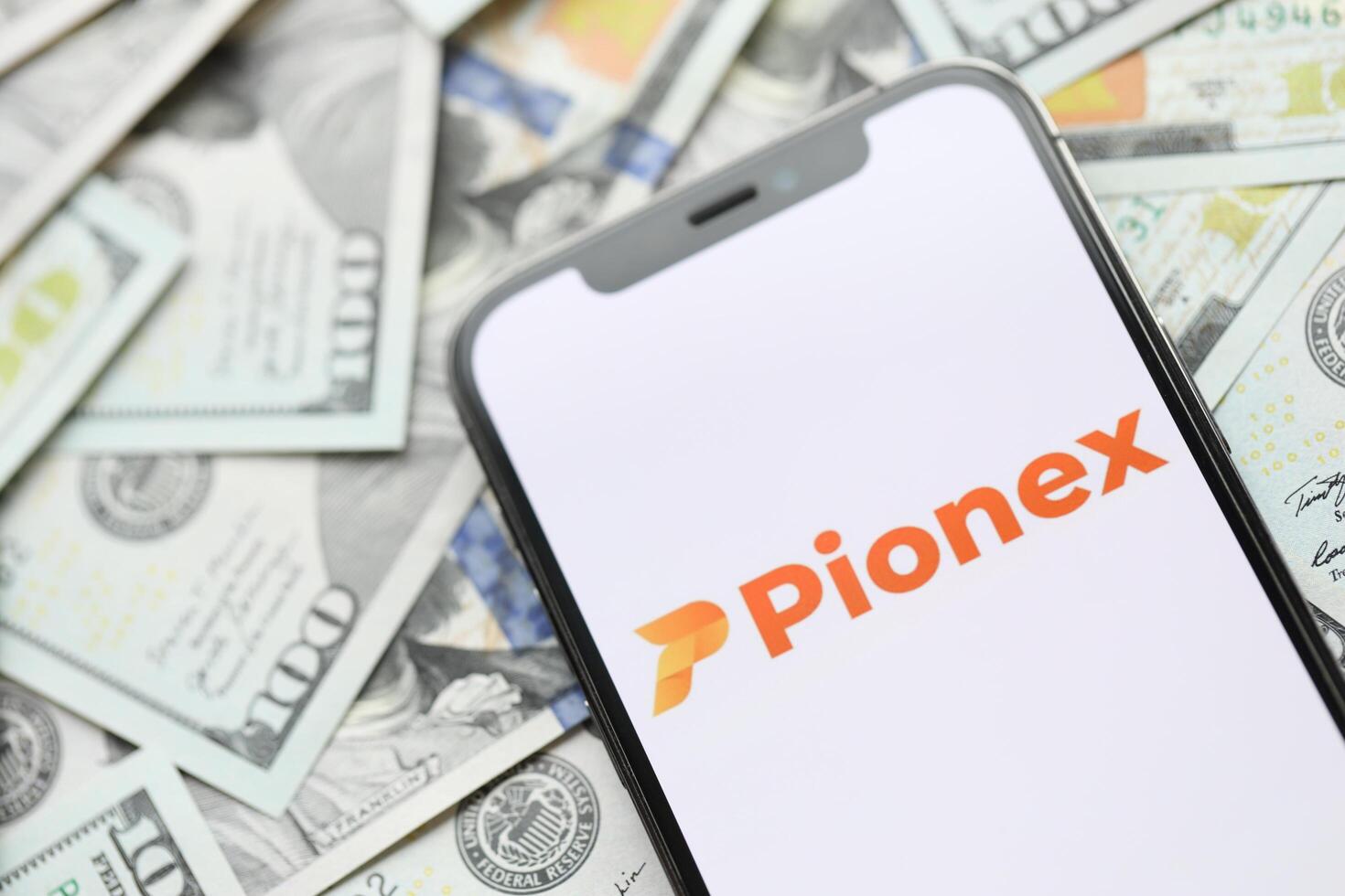 KYIV, UKRAINE - MARCH 15, 2024 Pionex logo on iPhone display screen with many hundred dollar bills photo