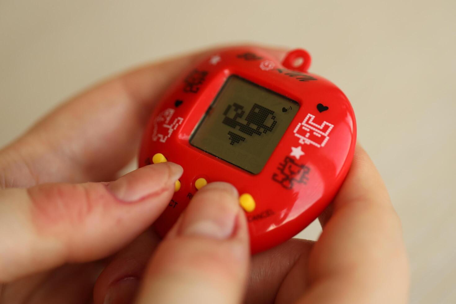 KYIV, UKRAINE - MARCH 9, 2024 Retro pet keychain game tamagotchi in red plastic case in female hands photo