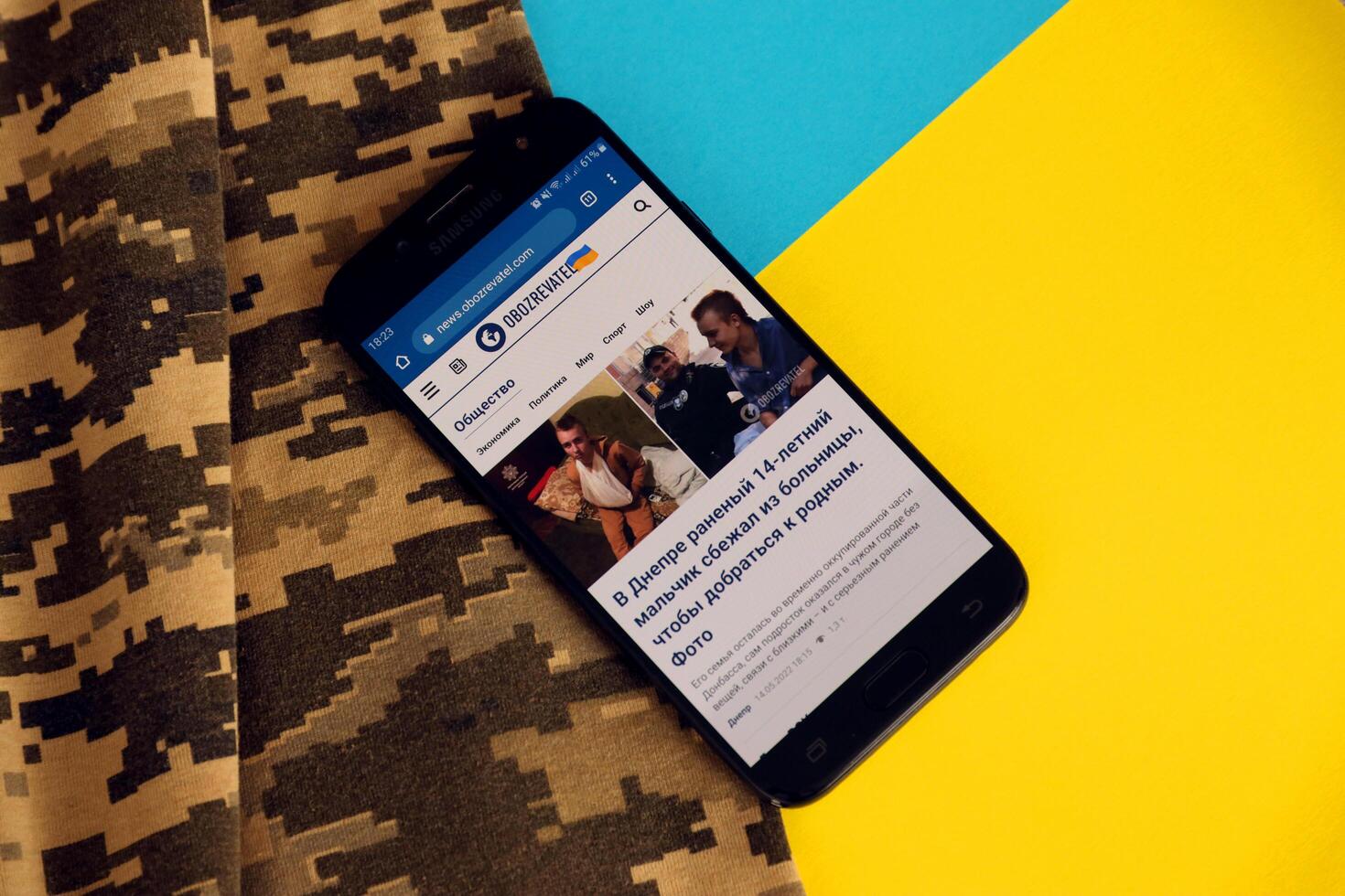 KYIV, UKRAINE - 4 MAY, 2023 Obozrevatel ukrainian news portal on smartphone screen with ukrainian flag and camouflage fabric photo