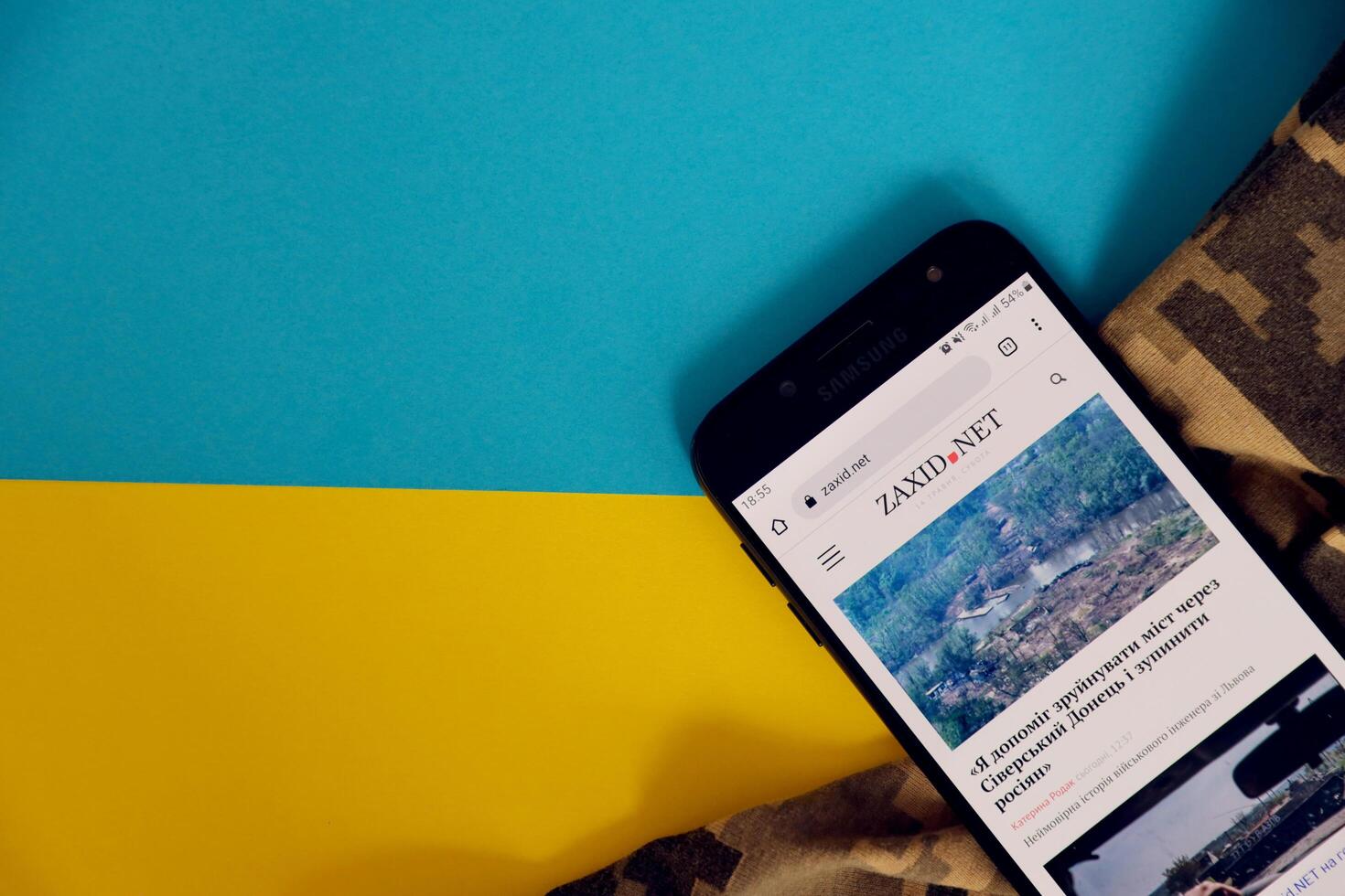 KYIV, UKRAINE - 4 MAY, 2023 Zaxid Net ukrainian news portal on smartphone screen with ukrainian flag and camouflage fabric photo