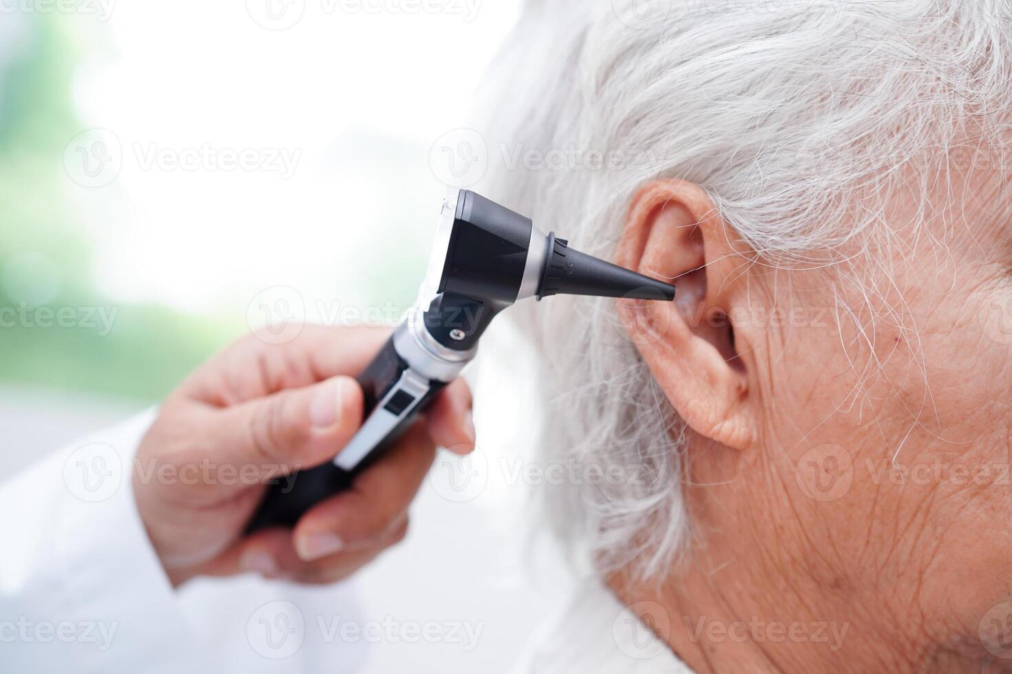 Otolaryngologist or ENT physician doctor examining senior patient ear with otoscope, hearing loss problem. photo