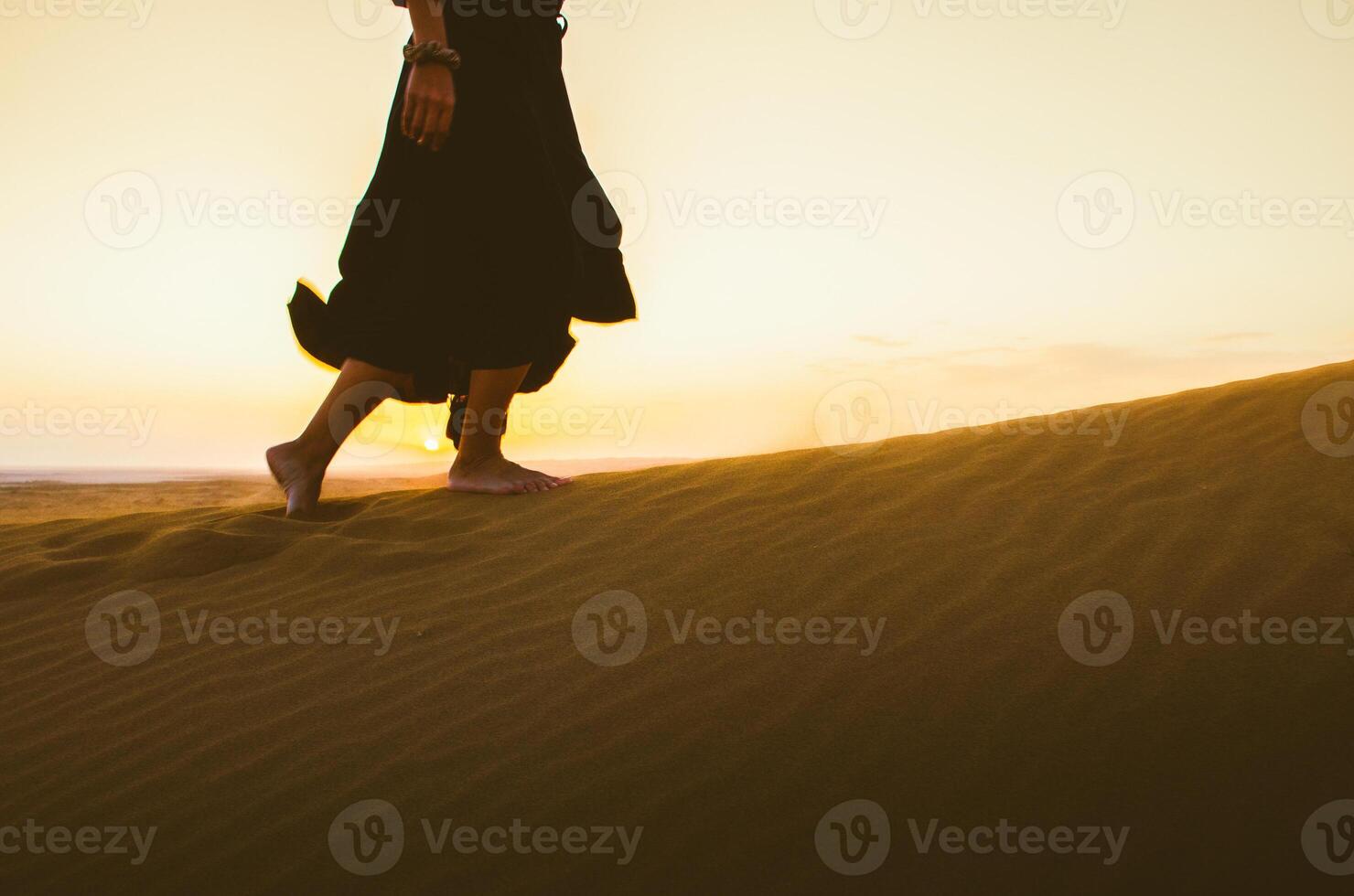 Low angle view iranian woman in long black dress feet walk on KAshan desert dunes with sunset background. Wanderlust concept mock up photo