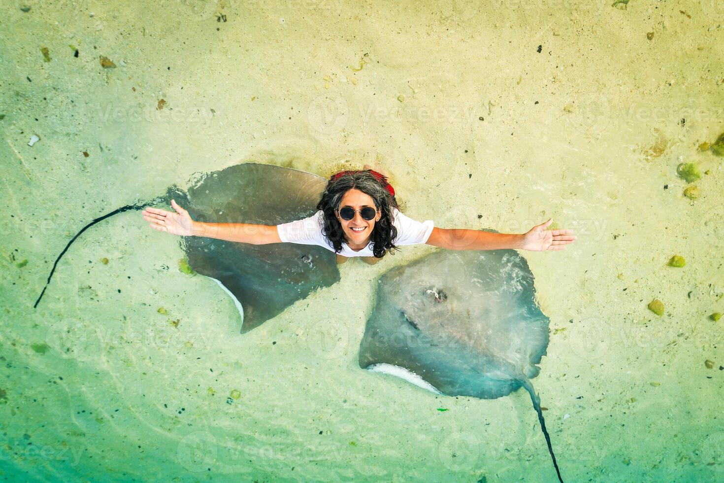 Aerial top down view caucasian woman excited pose raised arms enjoy company of stingrays on Maldives Fulidhoo island beach. Holiday vacation destination activities photo