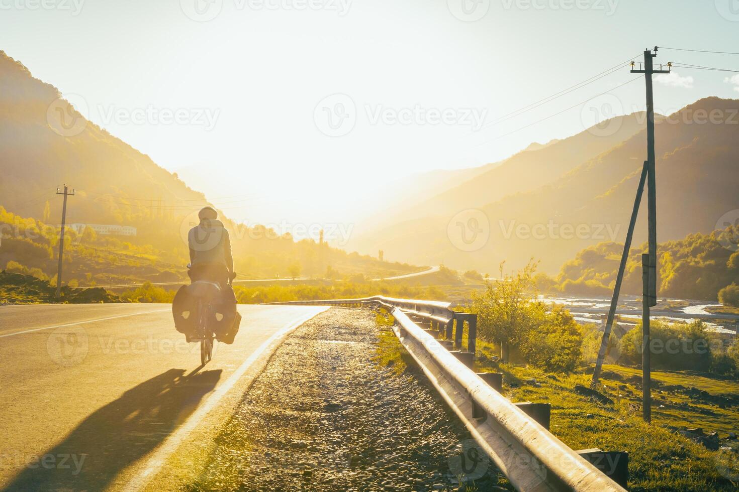Male cyclist on loaded touring bicycle ride on asphalt georgian road sign with caucasus mountains background on sunset. Travel Kazbegi national park. Adventurous travel background photo