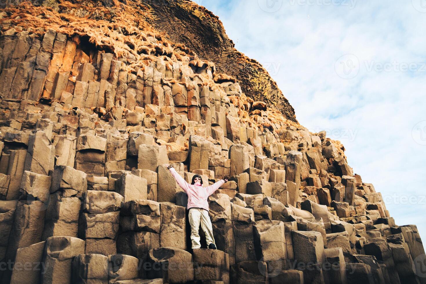 Iceland tourist at beach standing on basalt columns spread hands up on Reynisfjara beach, the black sand beach of Vik, South Iceland coast. Happy woman visiting tourist attraction photo