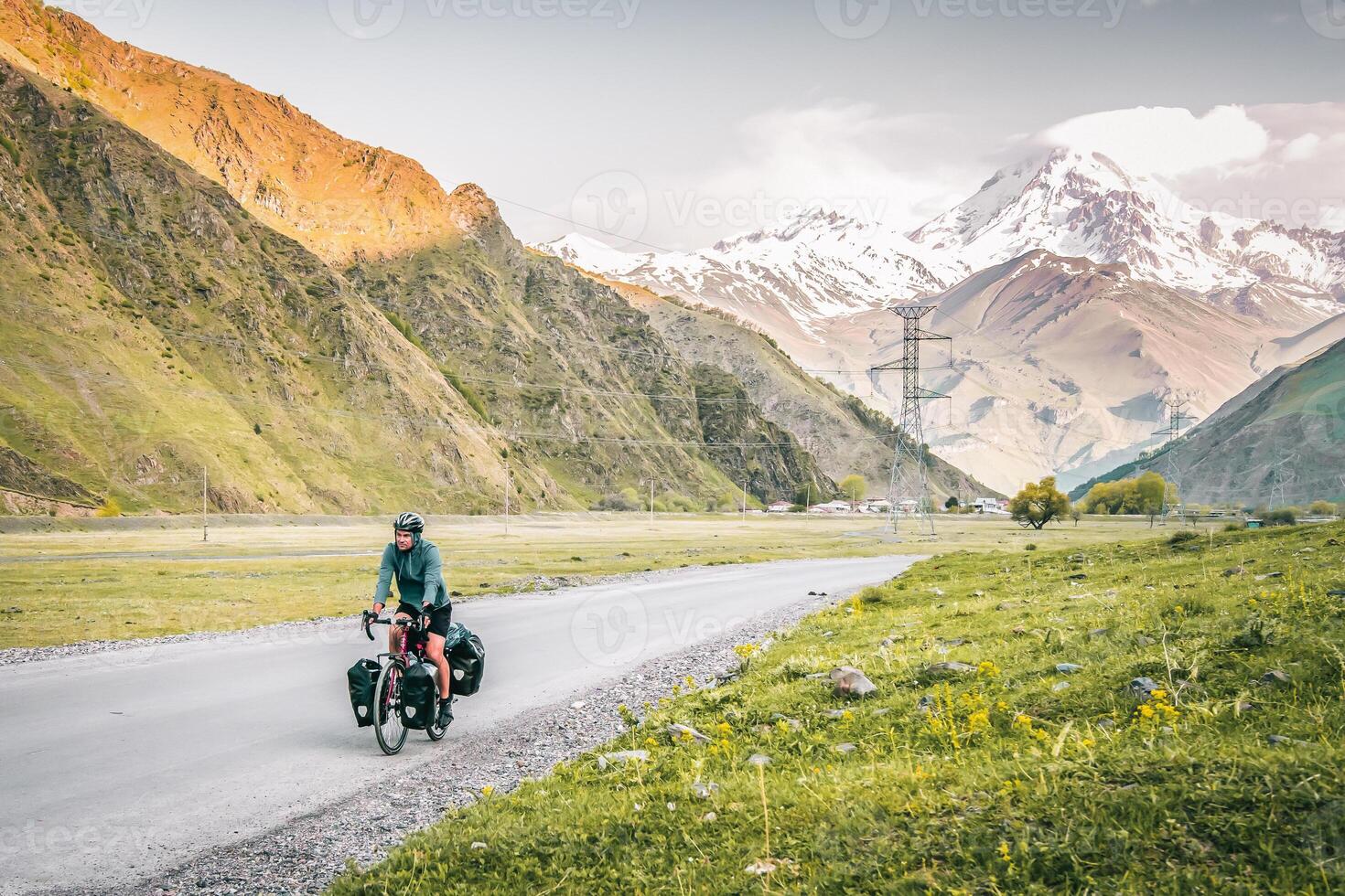 Caucasian male cyclist bicycle touring in caucasus KAzbegi mountains and Kazbek peak background. Travel around caucasus. Cycle around the world holidays outdoors photo