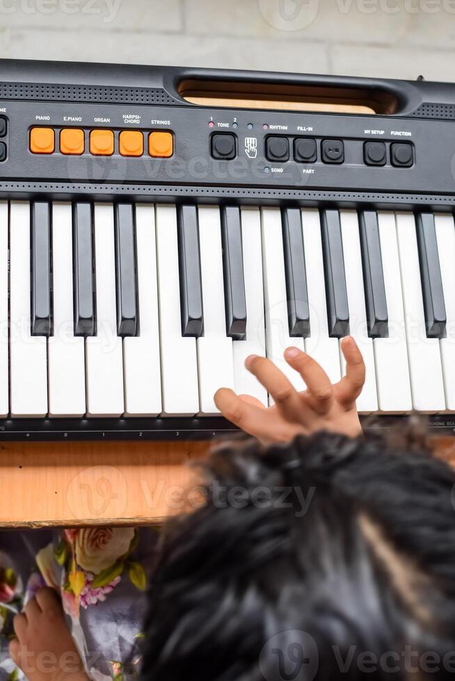 Asian cute girl playing the synthesizer or piano. Cute little kid learning how to play piano. Child's hands on the keyboard indoor. photo