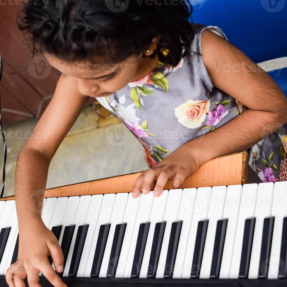Asian cute girl playing the synthesizer or piano. Cute little kid learning how to play piano. Child's hands on the keyboard indoor. photo