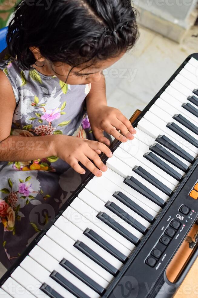 Asian cute girl playing the synthesizer or piano. Cute little kid learning how to play piano. Child's hands on the keyboard indoor. photo