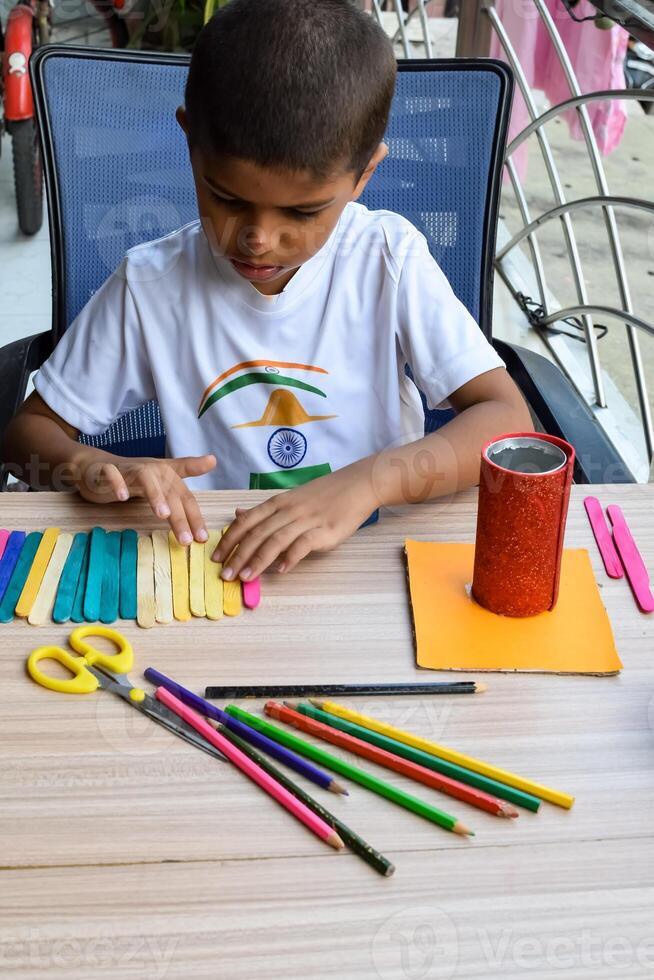 Smart Indian little boy performing best out of waste activity with different colourful objects during the summer vacations, Cute Indian Kid doing best our of waste activity at home on wooden table photo