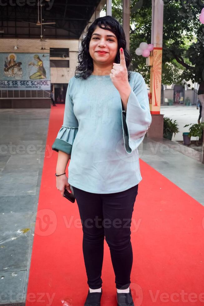 Smart young lady showing her ink-marked fingers after casting votes in front of polling booth of east Delhi area for general Lok Sabha Elections 2024 photo