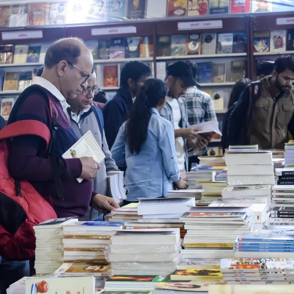 Delhi, India, May 17 2024 - Various age group people reading variety of Books on shelf inside a book-stall at Delhi International Book Fair, Books in Annual Book Fair at Bharat Mandapam complex photo