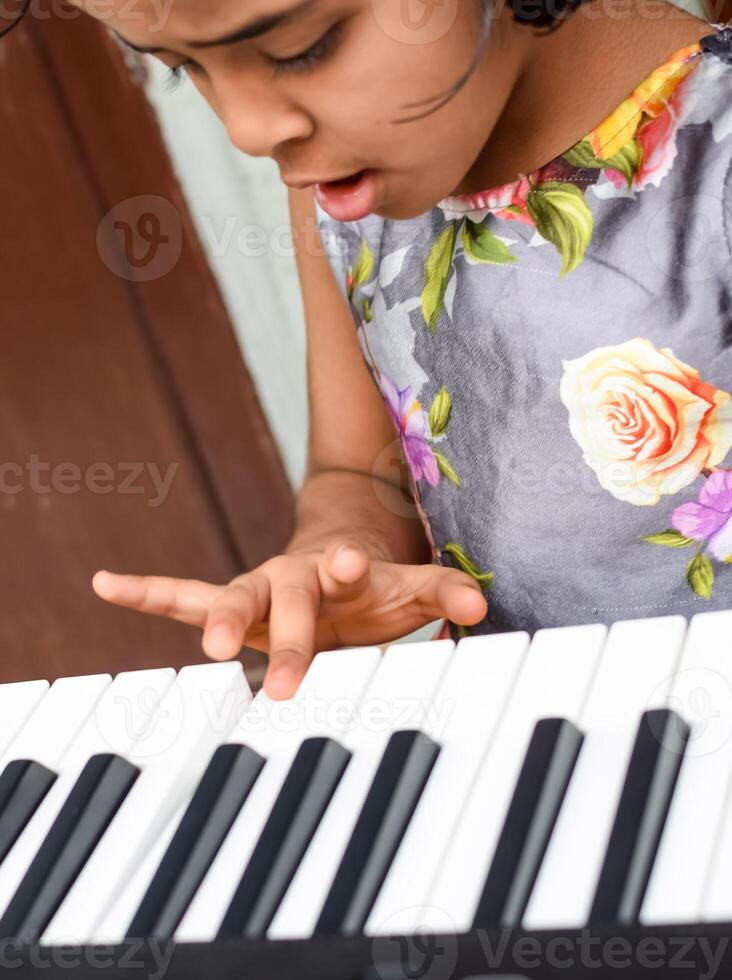 Asian cute girl playing the synthesizer or piano. Cute little kid learning how to play piano. Child's hands on the keyboard indoor. photo