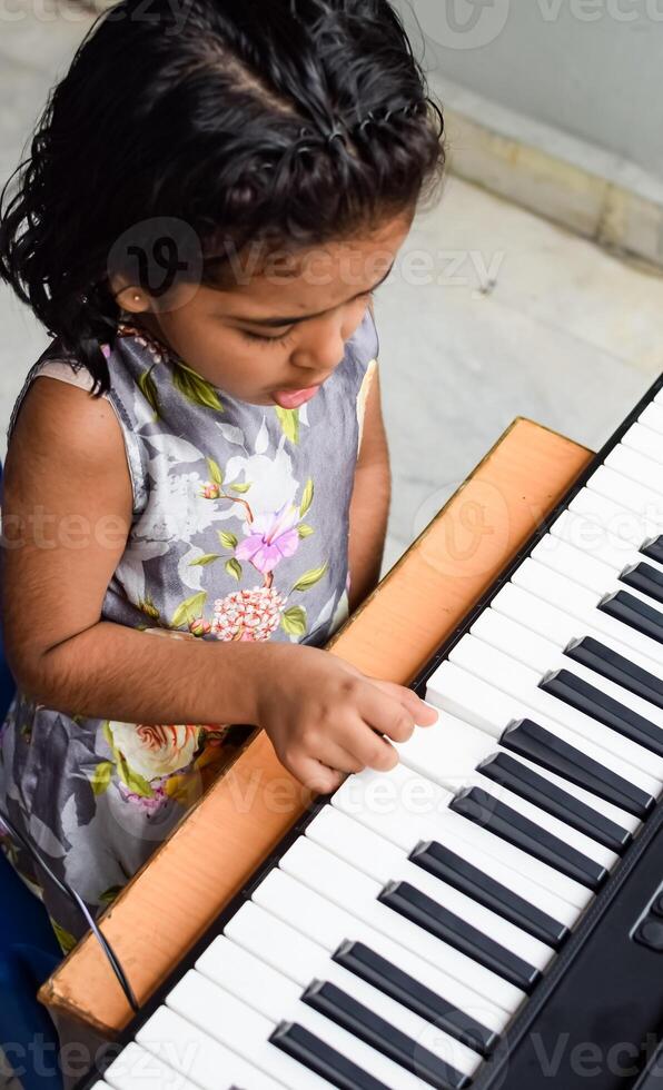 Asian cute girl playing the synthesizer or piano. Cute little kid learning how to play piano. Child's hands on the keyboard indoor. photo