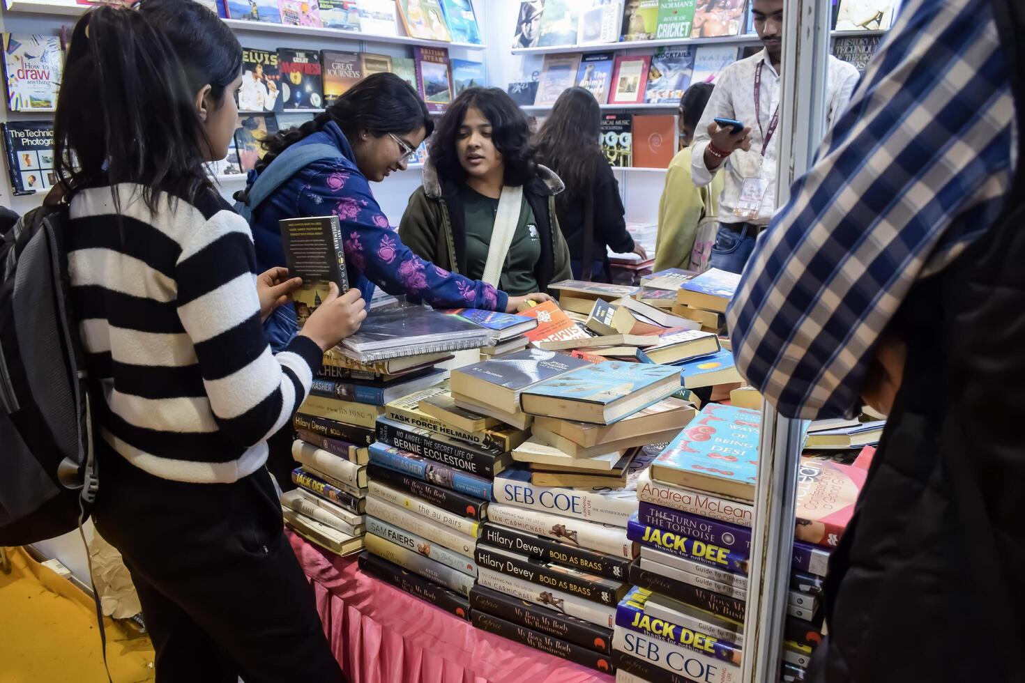 Delhi, India, May 11 2024 - Various age group people reading variety of Books on shelf inside a book-stall at Delhi International Book Fair, Books in Annual Book Fair at Bharat Mandapam complex photo