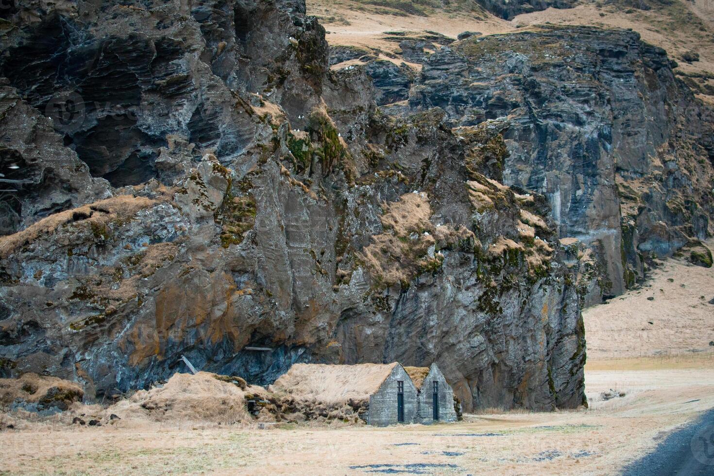 Turf house at foot of Drangurinn Rock in Southern Iceland. Eyjafjll mountains in southern Iceland near Ring Road, Route 1. Turfhouses linked to elves, folklore, sagas, and legends photo