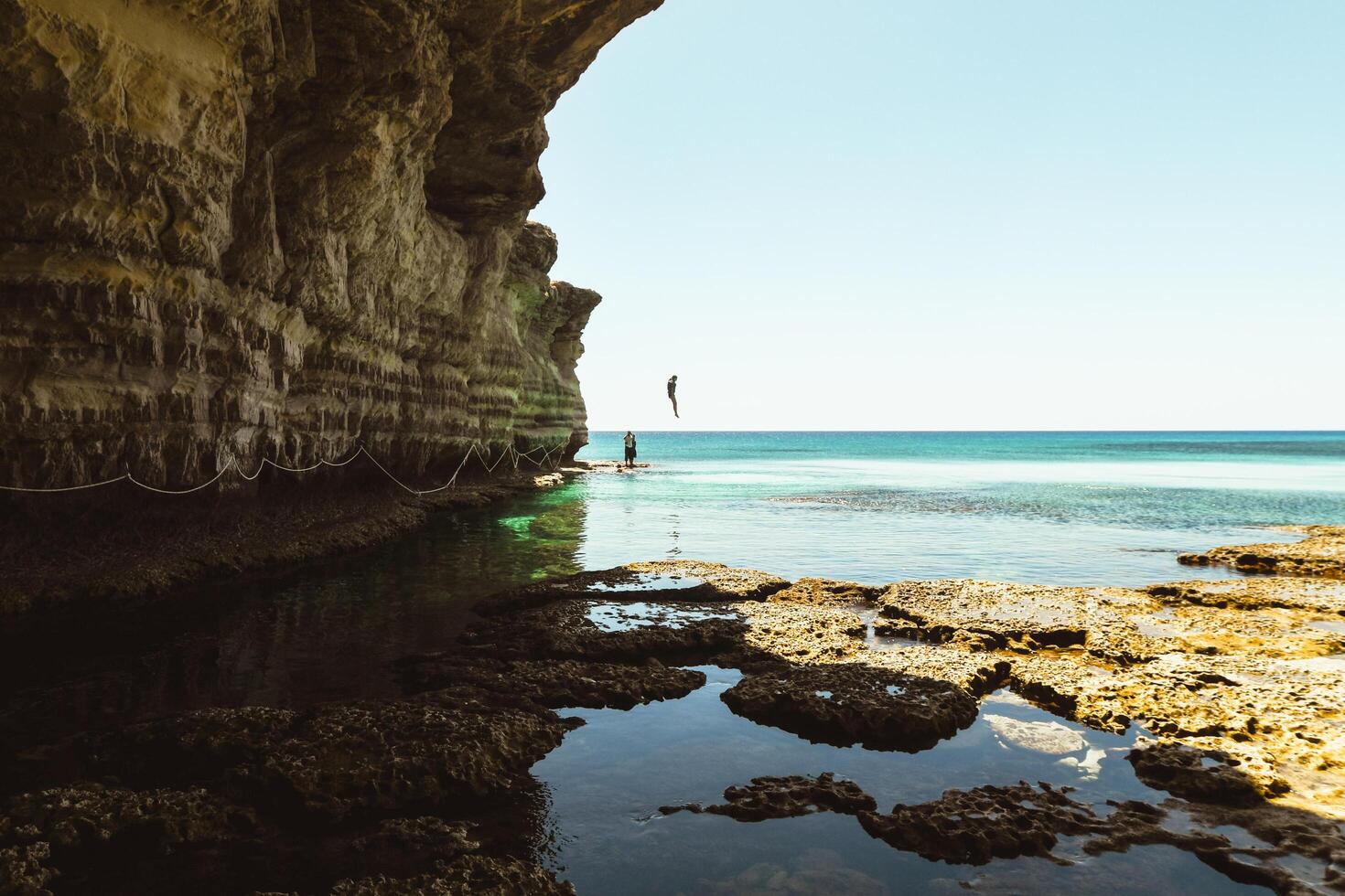Tourist jump in water Ayia napa bay shore with crystal blue mediterranean waters and tranquil rocky stone sea caves. Sightseeing path with ropes.Texture and islands geology concept photo